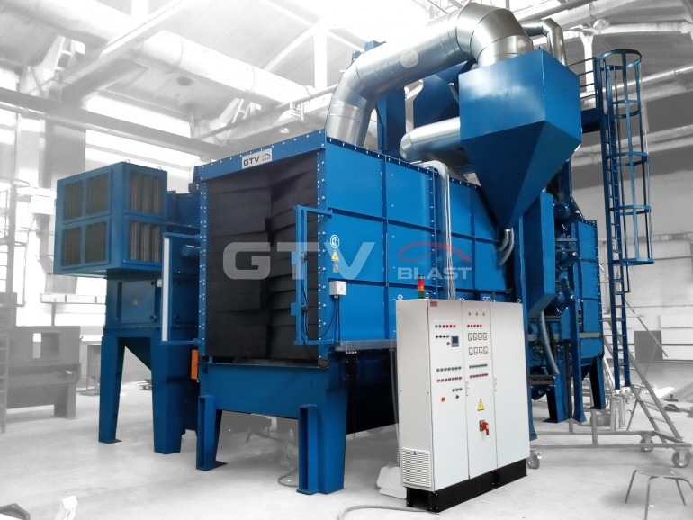 Duże, niebieskie urządzenie przemysłowe z rurami wentylacyjnymi i panelem sterowania, przeznaczone do linii produkcyjnej z malarnią i transportem pionowym, w hali o szarym tle.