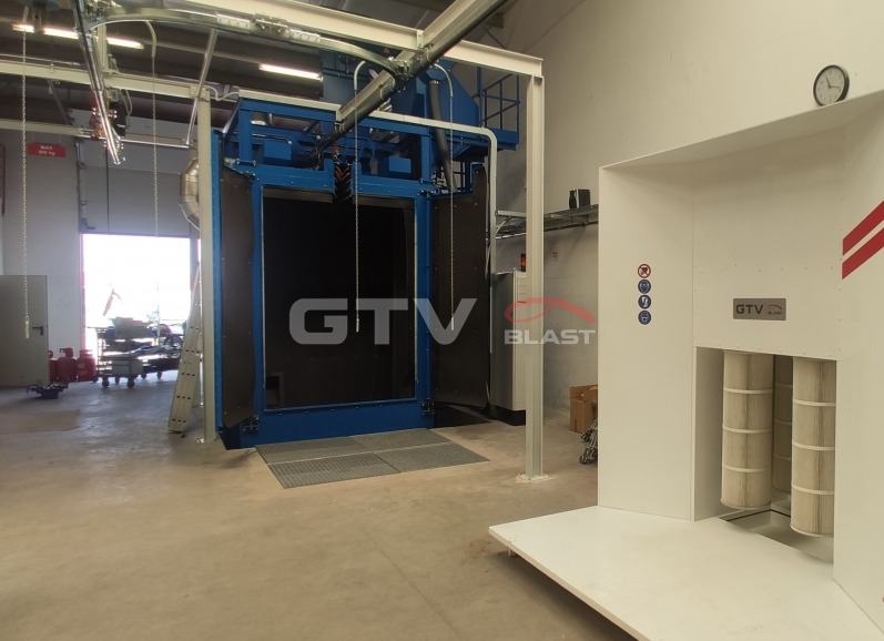 Komora śrutownicza GTV Blast z systemem transportu zawieszkowego, widoczna w hali produkcyjnej z otwartą bramą i filtrami powietrza.