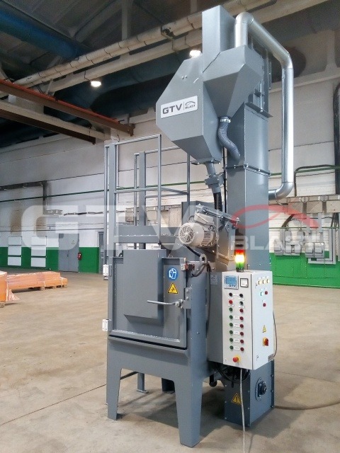 Widok na szarą, przemysłową śrutownicę wirnikową stołową w hali we Wrocławiu. Urządzenie posiada panel sterowania z wieloma przyciskami i lampkami sygnalizacyjnymi. Widoczna tabliczka ostrzegawcza.