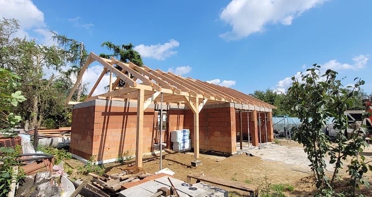 Wznoszenie konstrukcji dachu z drewna na budynku z czerwonej cegły, widok na niebo z chmurami.