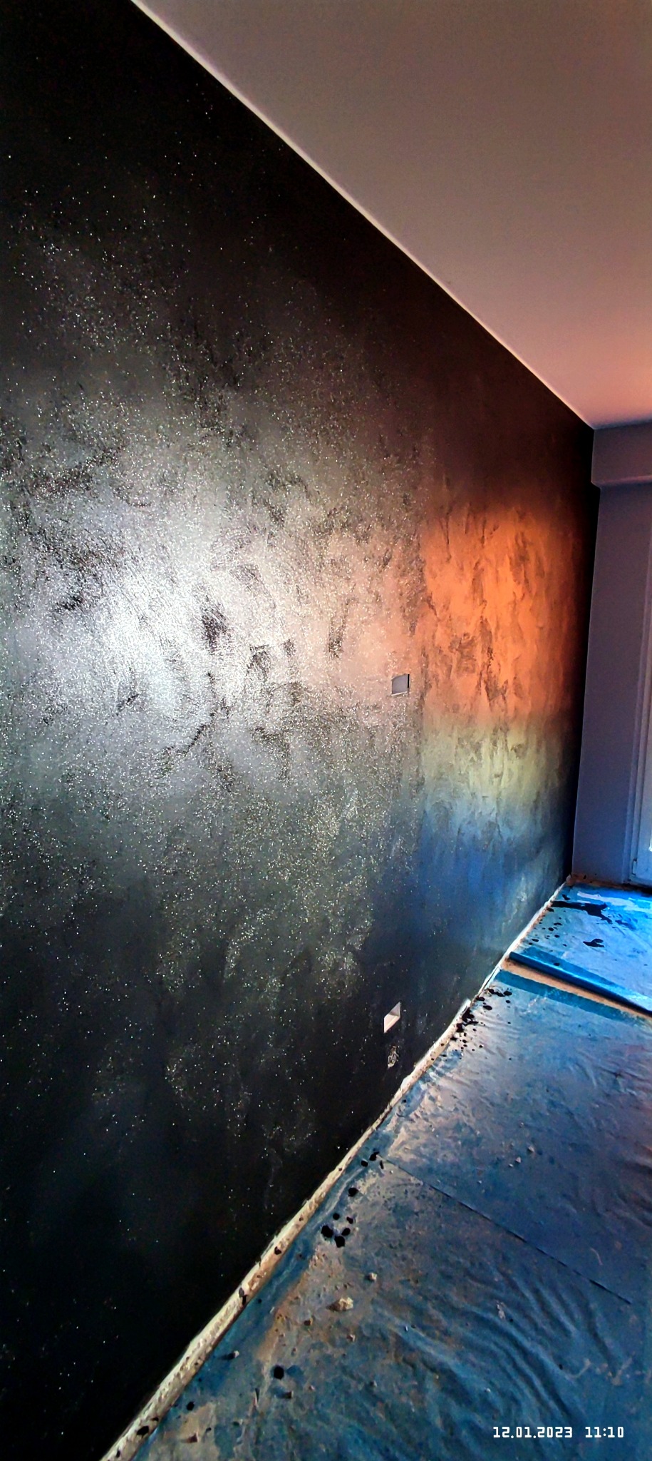 Ściana z efektem dekoracyjnym w odcieniach czerni i srebra, z widocznymi plamami i refleksami światła, zabezpieczona folią podłoga.