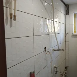 Białe płytki ścienne z fakturą w trakcie montażu w łazience, widoczne rury, poziomica i instalacja elektryczna.