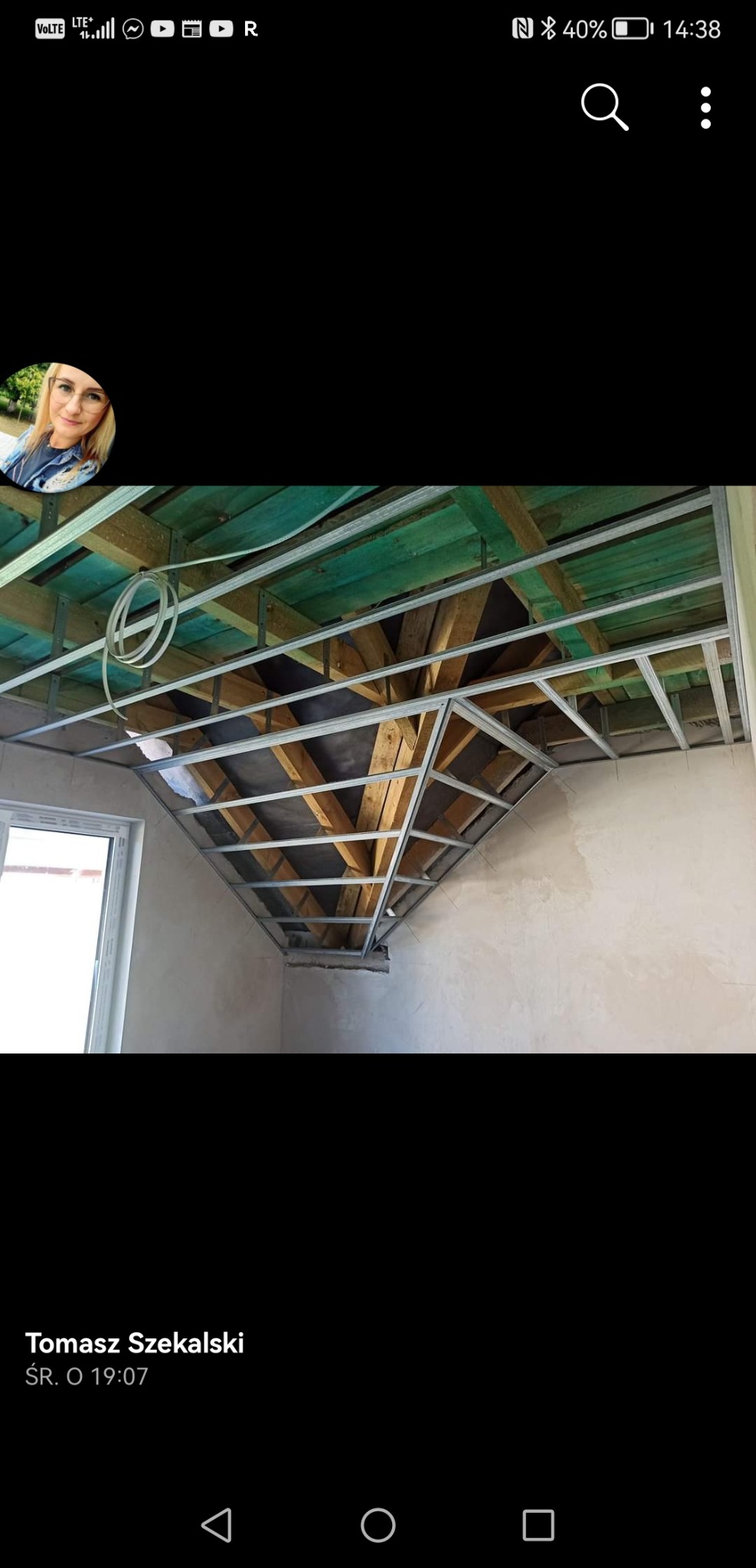 Konstrukcja sufitu podwieszanego z metalowych profili, widoczne drewniane belki stropowe, instalacja elektryczna i fragment okna w surowym wnętrzu