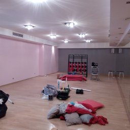 Malarz Pomorskie - Wnętrze sali fitness w trakcie remontu: różowe i szare ściany, parkiet w jasnym odcieniu, rozrzucone materiały budowlane i worki na śmieci, widoczne lustra na ścianie.