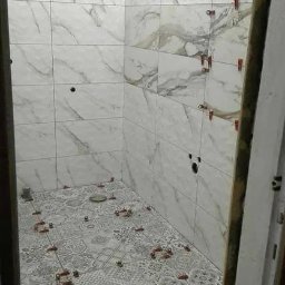 Usług budowlanych / praca/ wykończenia / itd - Łazienka w trakcie układania płytek podłogowych z wzorem patchworkowym i marmurowych płytek ściennych, widoczne krzyżyki dystansowe i otwory na instalacje.