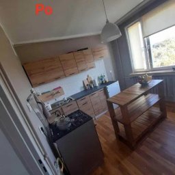Usług budowlanych / praca/ wykończenia / itd - Zdjęcie ukazuje wnętrze kuchni po remoncie, z widocznymi drewnianymi szafkami, ciemnym blatem, kuchenką gazową z garnkiem, drewnianym regałem i parkietem; w rogu widoczny napis 'Po'.