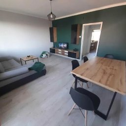 Usług budowlanych / praca/ wykończenia / itd - Jasne wnętrze pokoju dziennego z szarą sofą, drewnianym stołem z czarnymi krzesłami, ścianą w kolorze butelkowej zieleni i elementami dekoracyjnymi na ścianie.