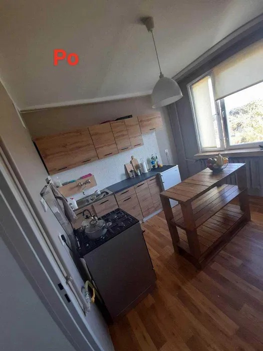 Zdjęcie ukazuje wnętrze kuchni po remoncie, z widocznymi drewnianymi szafkami, ciemnym blatem, kuchenką gazową z garnkiem, drewnianym regałem i parkietem; w rogu widoczny napis 'Po'.