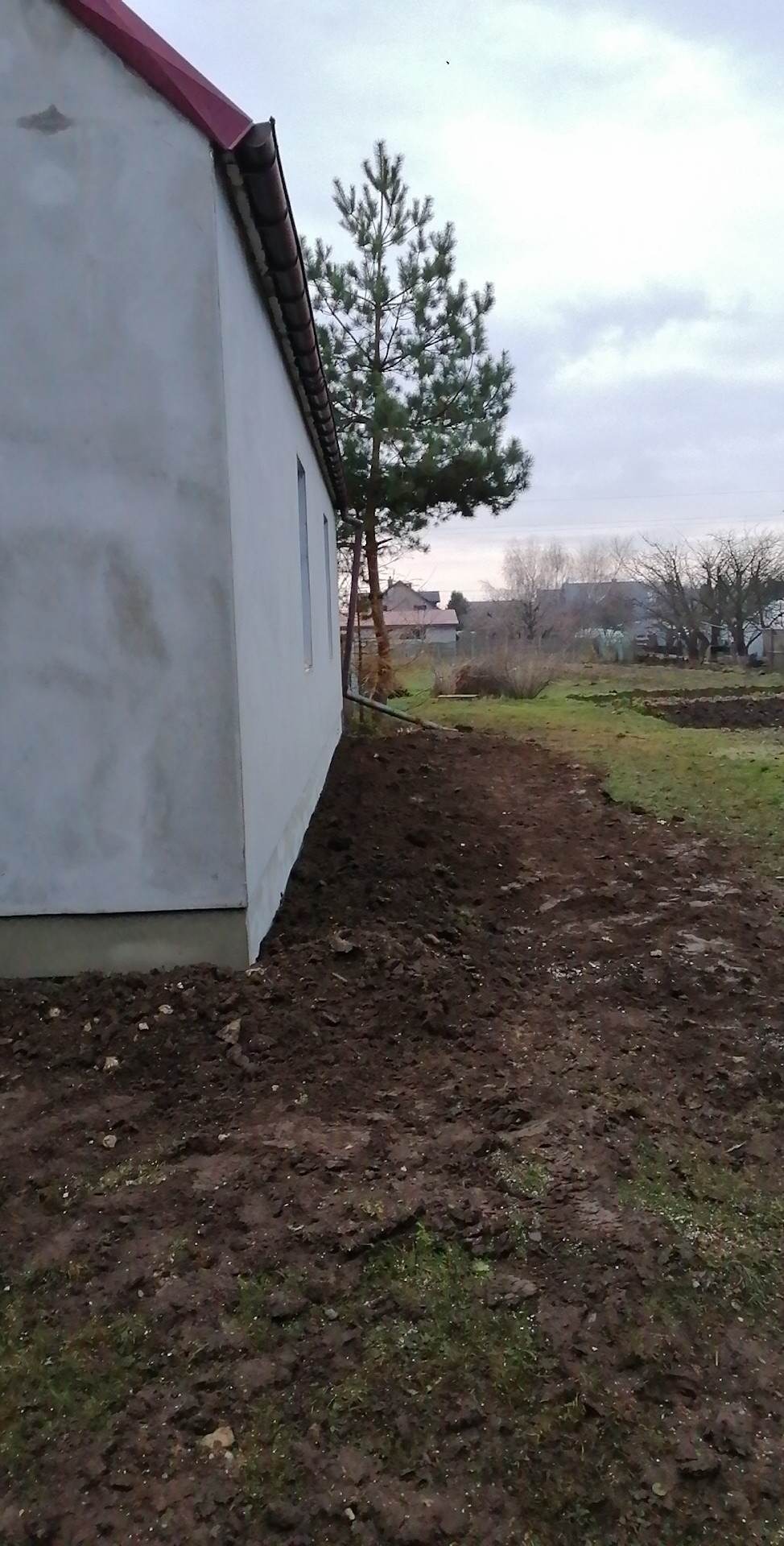 Świeżo otynkowana elewacja domu jednorodzinnego z widocznymi śladami po pracach, przygotowana do malowania, z obnażoną ziemią wokół fundamentów.