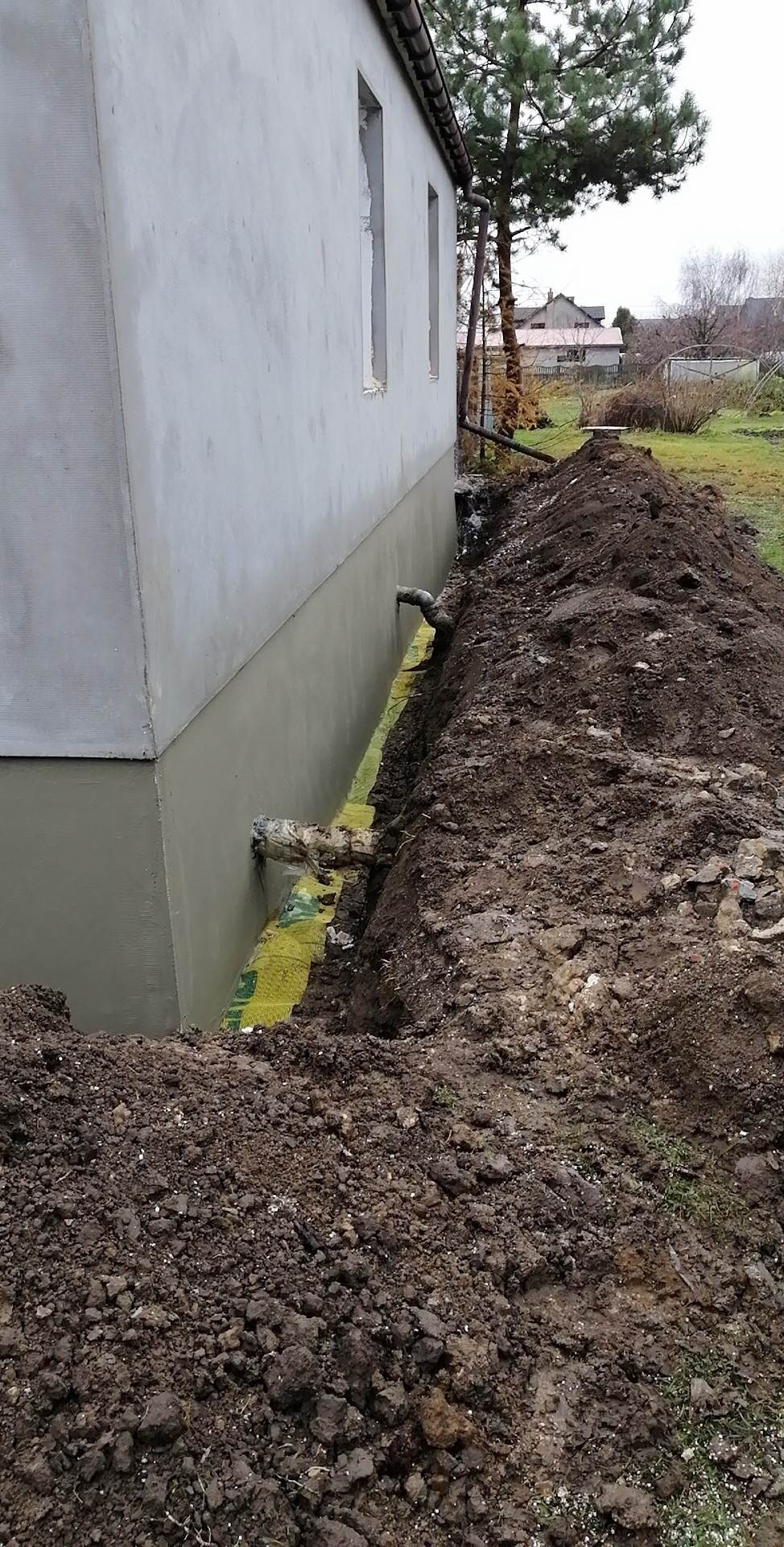 Fundament budynku po nałożeniu izolacji pionowej, widoczny wykop z żółtą folią izolacyjną i rurami odprowadzającymi wodę.