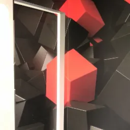 Wnętrze z tapetą w geometryczne wzory, dominują czarne i czerwone bloki 3D, widoczna biała framuga drzwi i fragment sufitu z kablem.