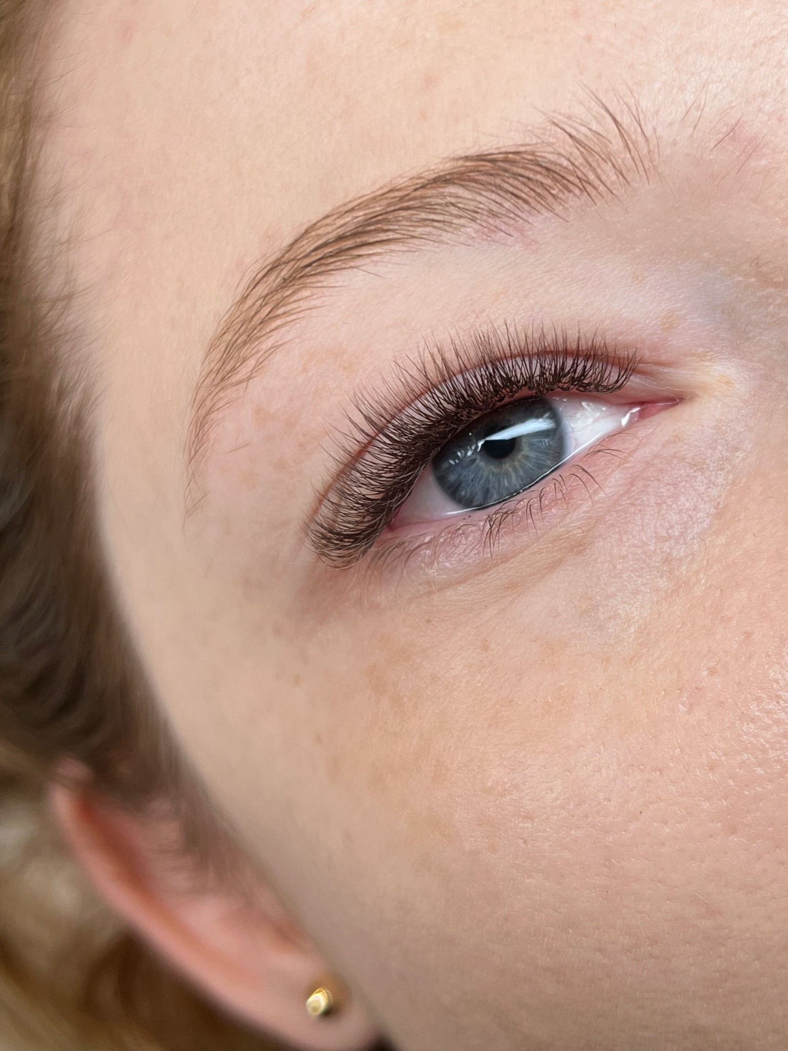 Zbliżenie na oko z przedłużonymi rzęsami w Nowym Sączu, widoczny subtelny makijaż i złoty kolczyk w uchu.