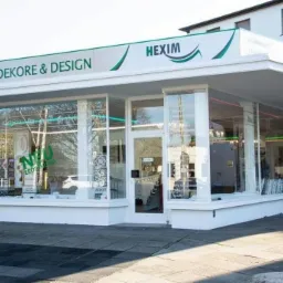 Fasada budynku firmy Dekore & Design Hexim z dużymi witrynami wystawowymi prezentującymi próbki dekoracji wnętrz i płytek ceramicznych.