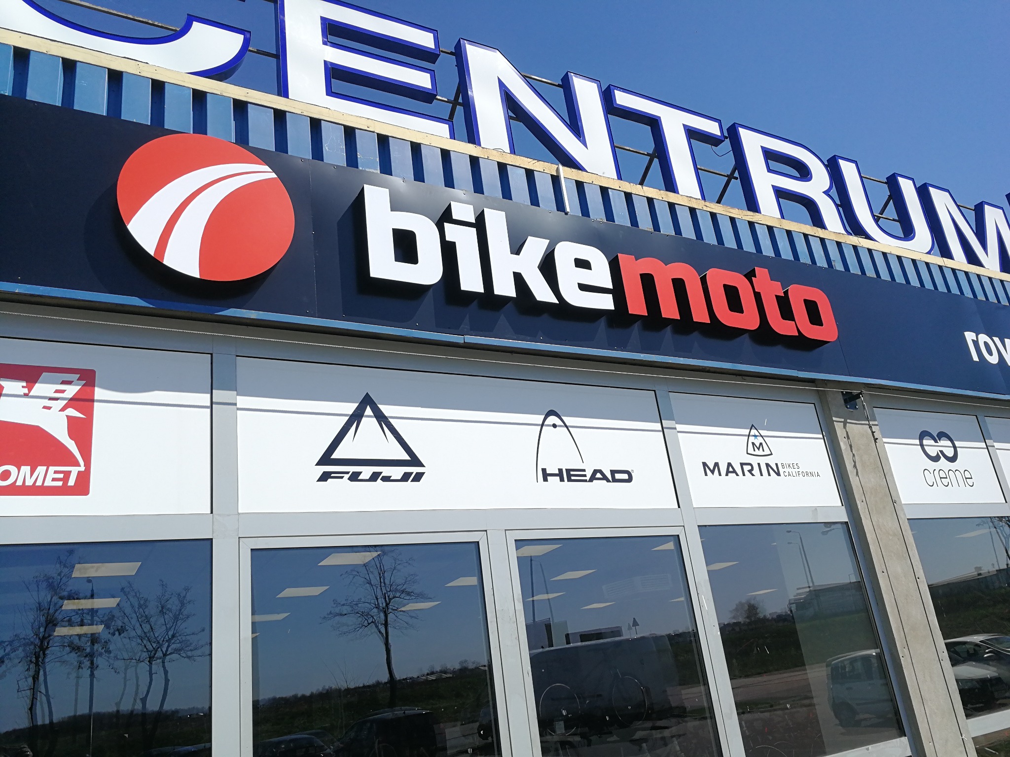 Elewacja sklepu rowerowego BikeMoto Centrum z logo różnych marek rowerowych (Comet, Fuji, Head, Marin, Creme) na witrynach.