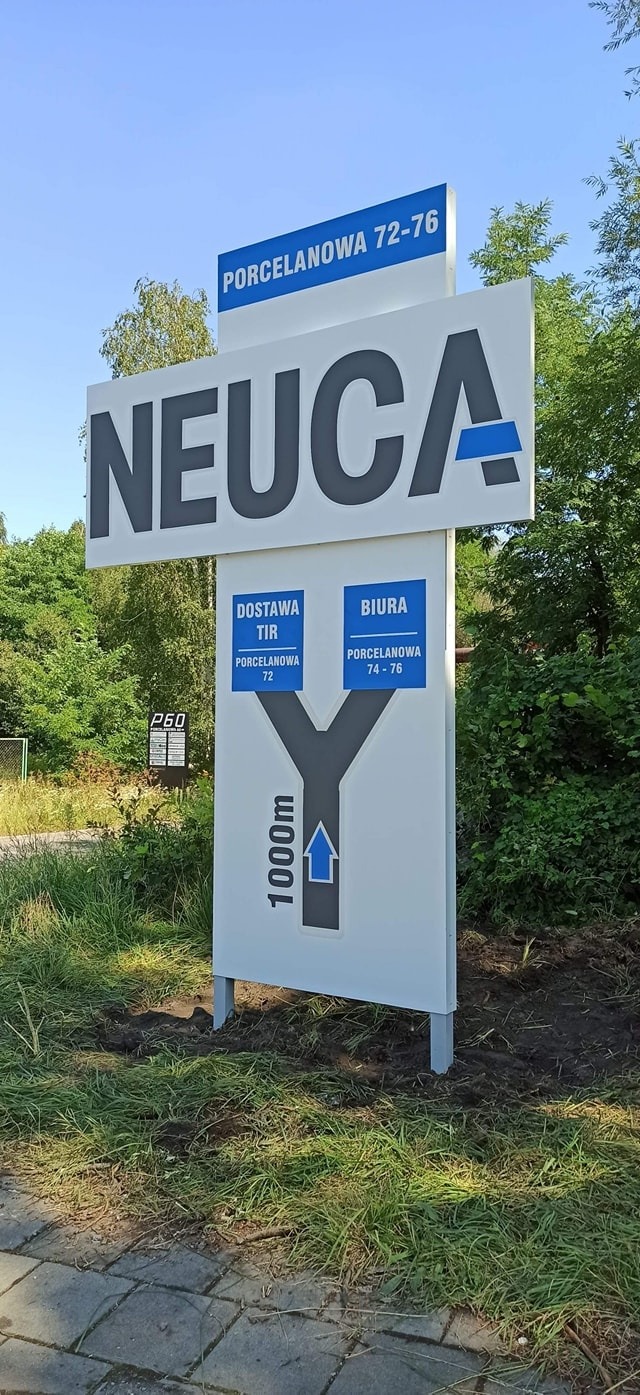 Pylon reklamowy z nazwą firmy NEUCA, informacją o adresie (Porcelanowa 72-76) oraz wskazówkami dojazdu do biura i dostawy TIR, umieszczony na zewnątrz budynku na tle zieleni.
