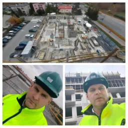 Kask BHP na głowie mężczyzny w jaskrawej kurtce na tle budowy w stanie surowym, widok z góry na plac budowy z betoniarką i samochodami w tle.