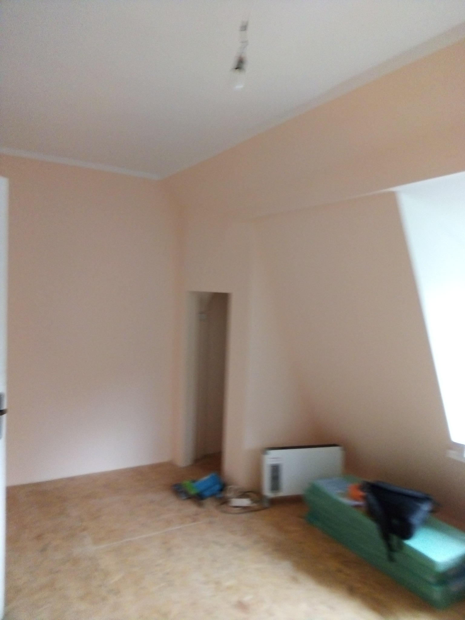 Pokój z pomalowanymi na jasny róż ścianami i przygotowanym podłożem pod podłogę, widoczny grzejnik i materiały izolacyjne.