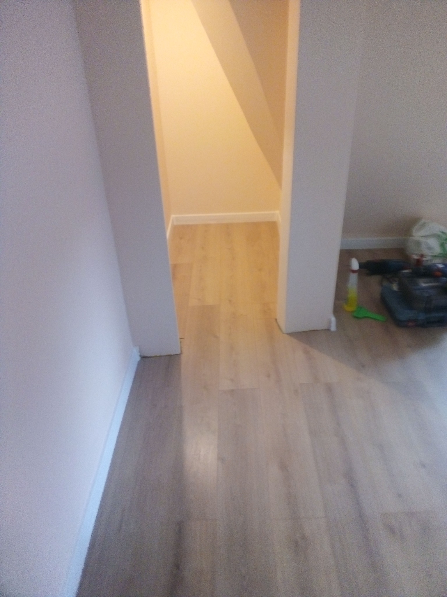 Nowo położone panele podłogowe w wąskim przejściu, widoczne narzędzia i akcesoria w rogu pomieszczenia.