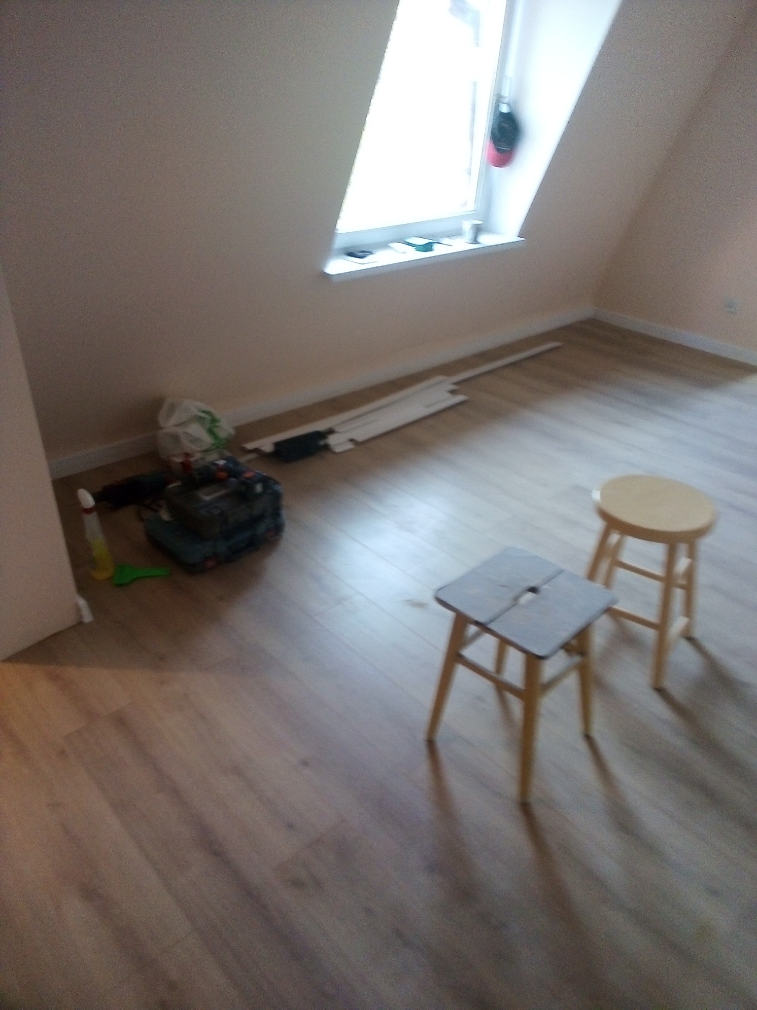 Poddasze po remoncie z nową podłogą z paneli, widoczne dwa taborety, narzędzia i listwy przypodłogowe przygotowane do montażu.