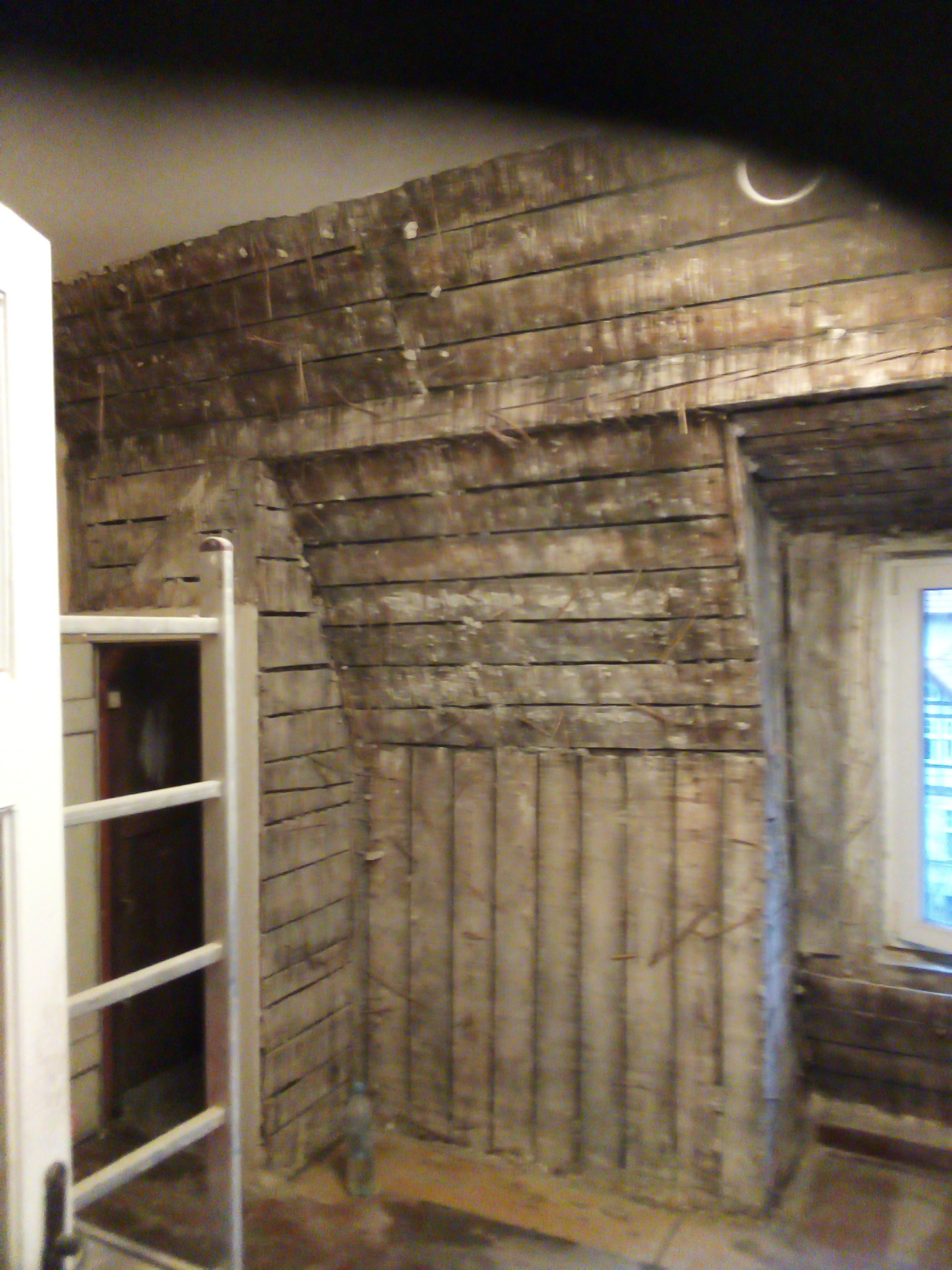 Poddasze w trakcie przygotowania do ocieplenia: widoczne drewniane legary, ślady po usuniętej izolacji, okno w ścianie szczytowej i biała drabina oparta o ścianę.