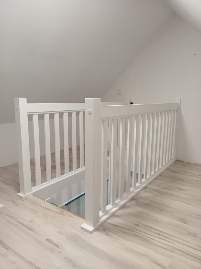 Biała balustrada antresoli z widocznym wejściem na niższy poziom, wykończona w minimalistycznym stylu, na podłodze panele imitujące drewno.