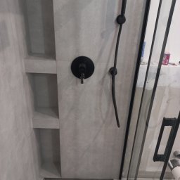 Otobud - Szara łazienka z czarną armaturą: bateria prysznicowa z deszczownicą, wbudowane półki w ścianie, odpływ liniowy i szklana kabina prysznicowa z czarnymi profilami.