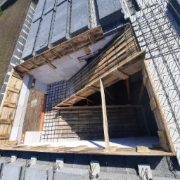 Widok z góry na konstrukcję dachu w trakcie budowy, z widocznym szalunkiem z desek, siatką zbrojeniową i bloczkami betonowymi.