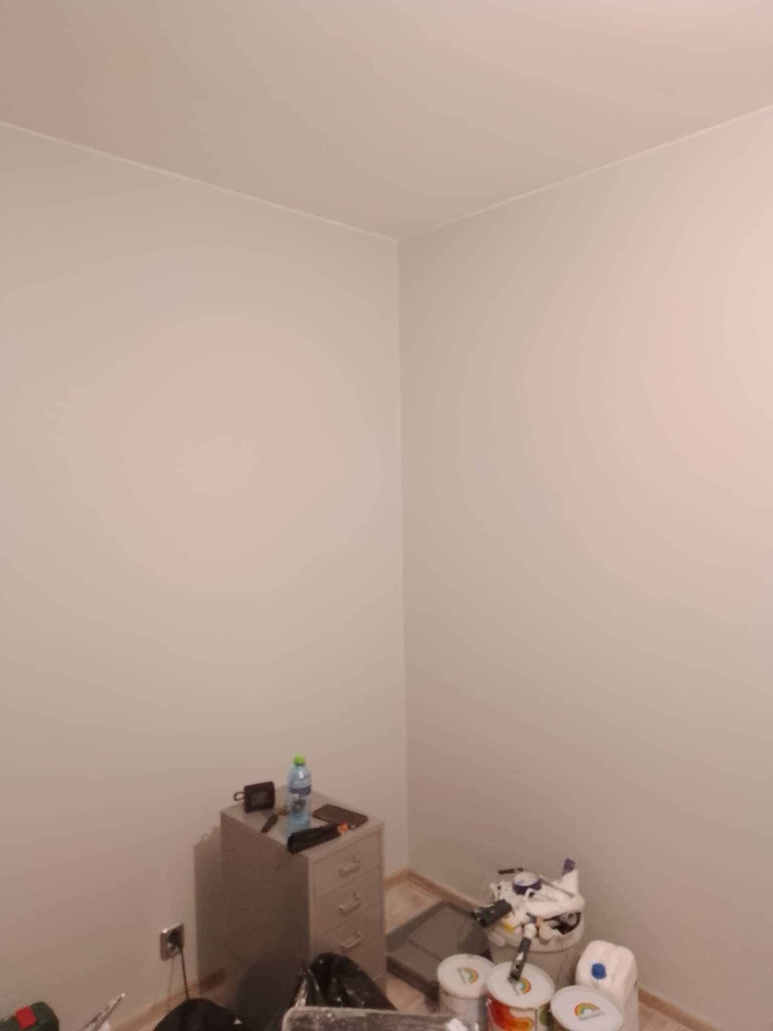 Świeżo pomalowane na jednolity jasny kolor ściany w pomieszczeniu w Pruszczu Gdańskim, widoczne puszki z farbą i akcesoria malarskie.