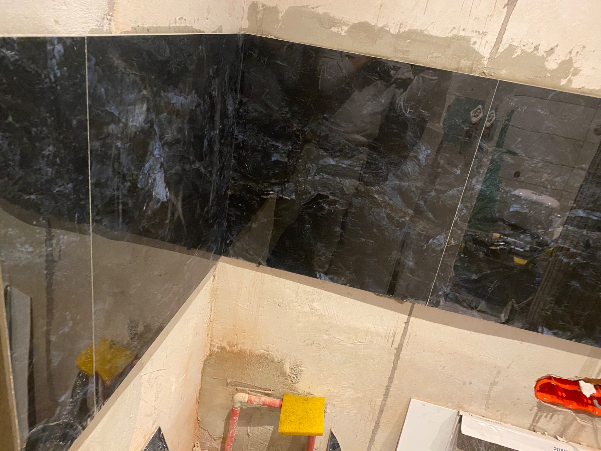 Fragment łazienki w trakcie remontu: czarne płytki imitujące marmur na ścianie, widoczne ślady po kleju i gąbka do czyszczenia fug.