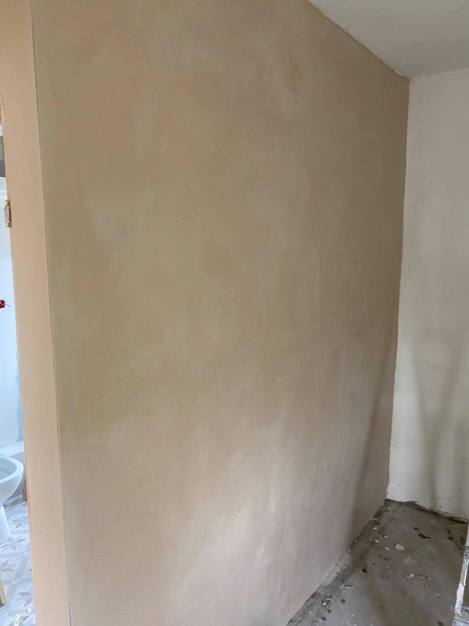 Ściana po nałożeniu szpachli, widoczne nierówności przed szlifowaniem, surowy beton na podłodze.