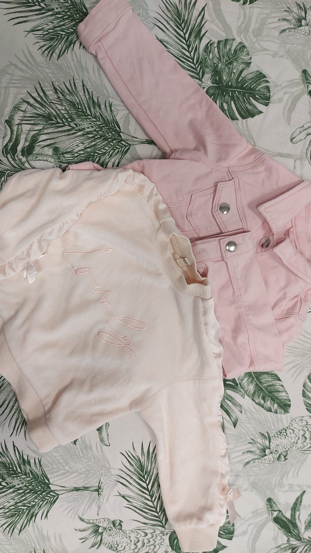 Dwa elementy damskiej garderoby w odcieniach różu: dzinsowa kurtka i bluza z napisem 'Lovely' na tle tkaniny w tropikalne liście.