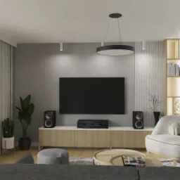 Nowoczesny salon z szarą ścianą, telewizorem, drewnianą szafką RTV, głośnikami, okrągłym stolikiem kawowym i fotelem w odcieniach szarości, oświetlony wiszącą lampą pierścieniową.