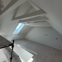 Poddasze w Strzebielinie po malowaniu na biało, widoczne drewniane belki stropowe, okno dachowe i fragment rusztowania.