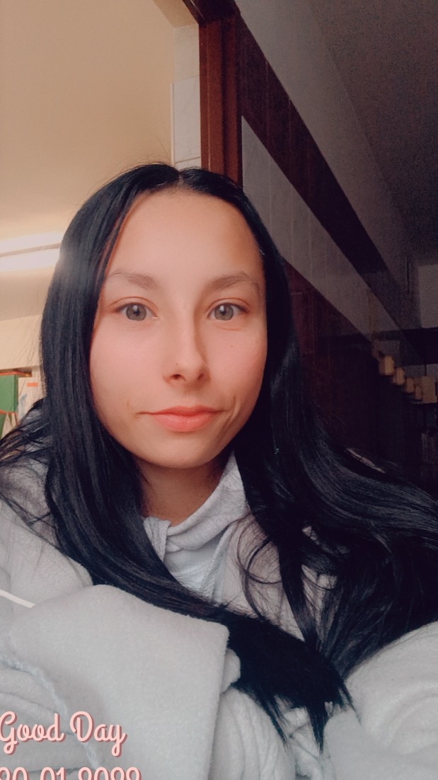 Portret młodej kobiety z długimi, czarnymi włosami, ubranej w szarą bluzę z kapturem, otulonej białym kocem, z napisem 'Good Day 20.01.2022' w rogu zdjęcia.