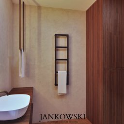 Szymon Jankowski - Nowoczesna łazienka z podświetlanym lustrem, umywalką nablatową i drewnianą szafą. Minimalistyczny design z akcentami brązu i beżu. Grzejnik drabinkowy z ręcznikiem.