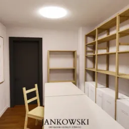 Jasne biuro z drewnianymi regałami i minimalistycznymi grafikami. Krzesło przy biurku, czarne drzwi. Stonowana kolorystyka, nowoczesny design.