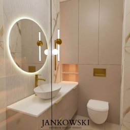 Szymon Jankowski - Elegancka łazienka z okrągłym lustrem LED, złotą armaturą i marmurowymi płytkami. Minimalistyczny design z podświetlanymi niszami.