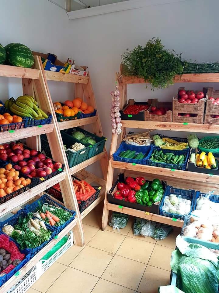 Drewniane regały wypełnione świeżymi owocami i warzywami w sklepie, z czosnkiem wiszącym na boku i kafelkami na podłodze.
