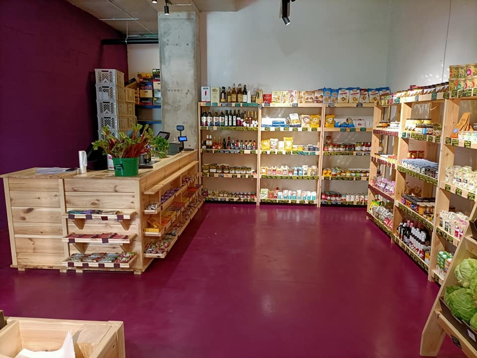 Wnętrze sklepu ze zdrową żywnością: drewniane regały i lada z naturalnego drewna, fioletowa podłoga, ekspozycja produktów.