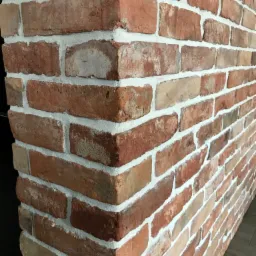 Dekoracyjna ściana z czerwonej cegły z fugami w kolorze złamanej bieli, widoczny narożnik i fragment podłogi.