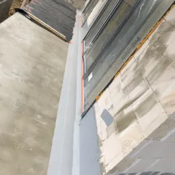 Widok z góry na fragment elewacji w trakcie ocieplania, z widoczną siatką zabezpieczającą, pianką montażową oraz częściowo pomalowaną powierzchnią.