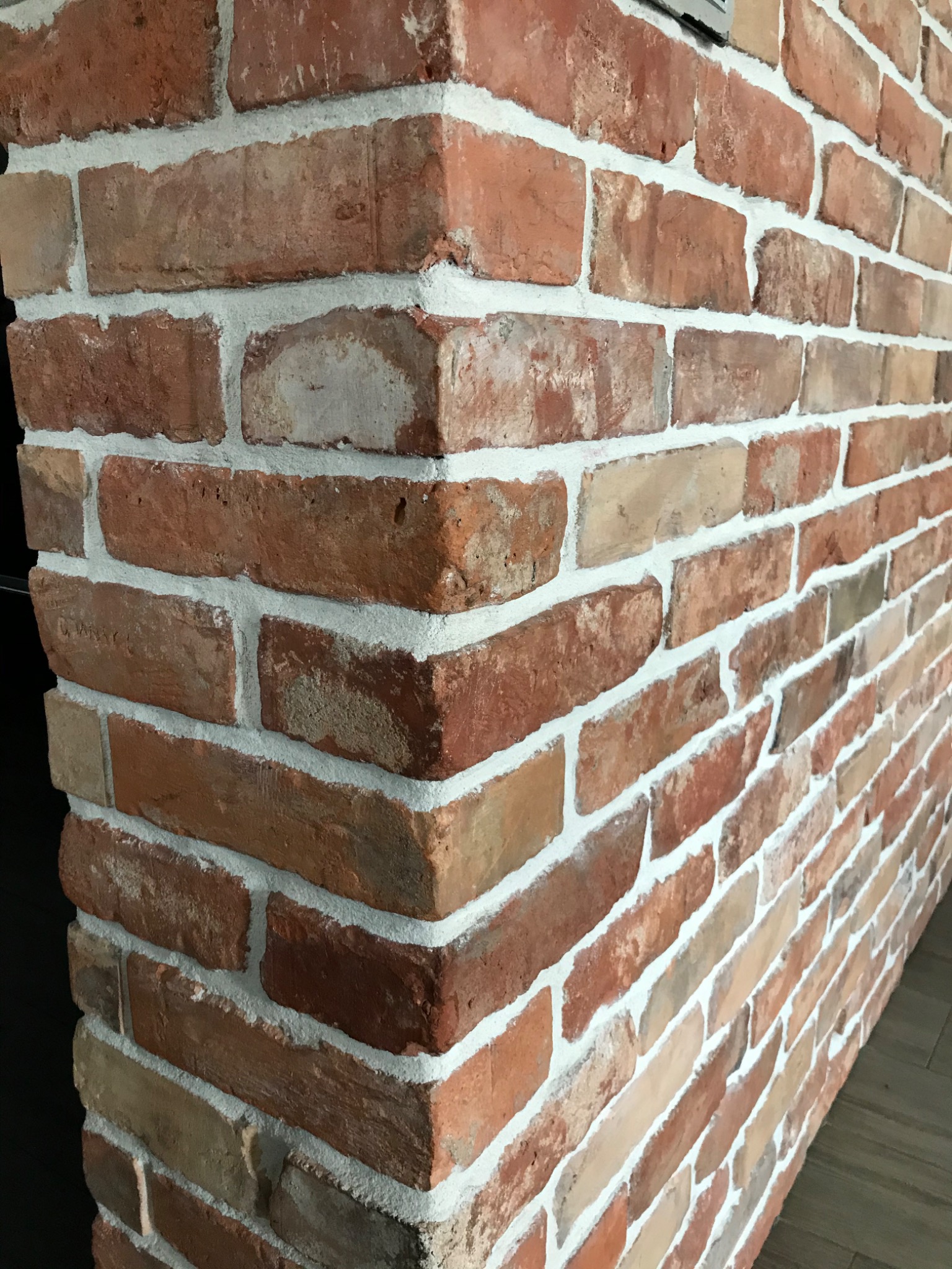 Dekoracyjna ściana z czerwonej cegły z fugami w kolorze złamanej bieli, widoczny narożnik i fragment podłogi.