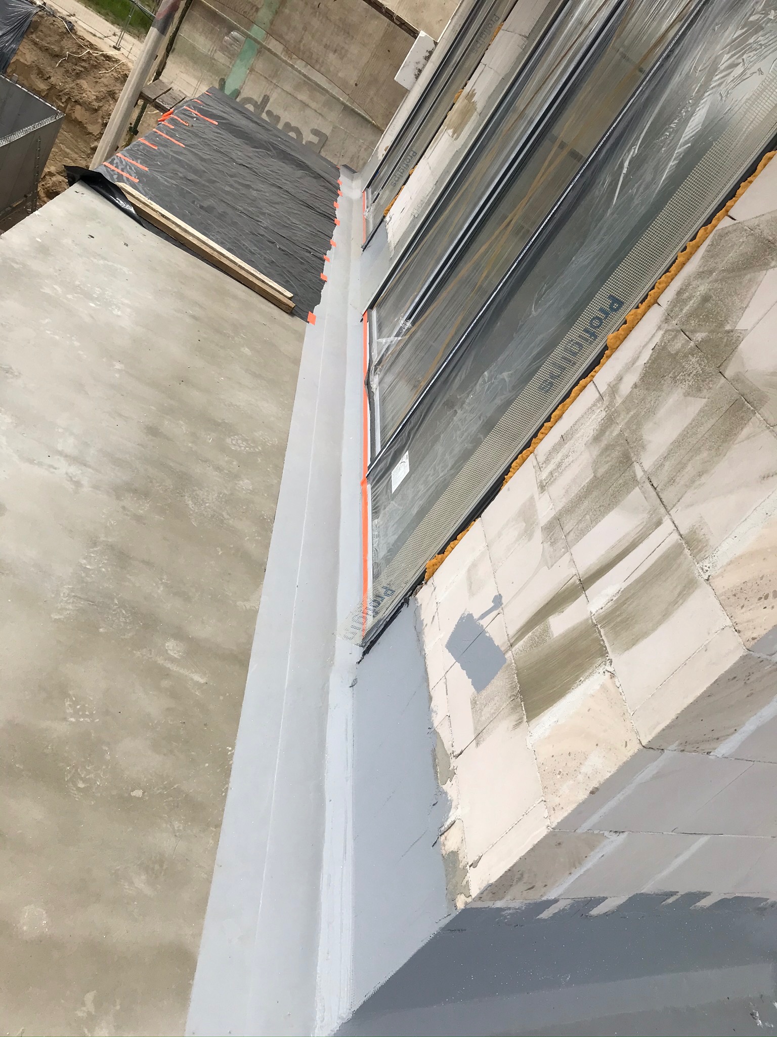 Widok z góry na fragment elewacji w trakcie ocieplania, z widoczną siatką zabezpieczającą, pianką montażową oraz częściowo pomalowaną powierzchnią.