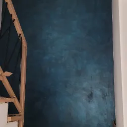 Ściana w odcieniach granatu i błękitu z efektem ombre, widoczna obok drewnianych schodów zabezpieczonych folią i kartonem w trakcie prac wykończeniowych.