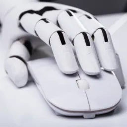 Biała, przegubowa dłoń robota spoczywa na białej myszce komputerowej, sugerując automatyzację procesów biurowych.