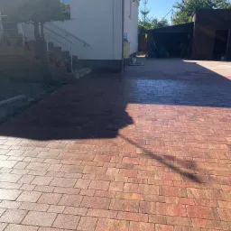 Nowo ułożona, czerwono-brązowa kostka brukowa na podjeździe przed domem z numerem 4, w tle widoczny garaż.