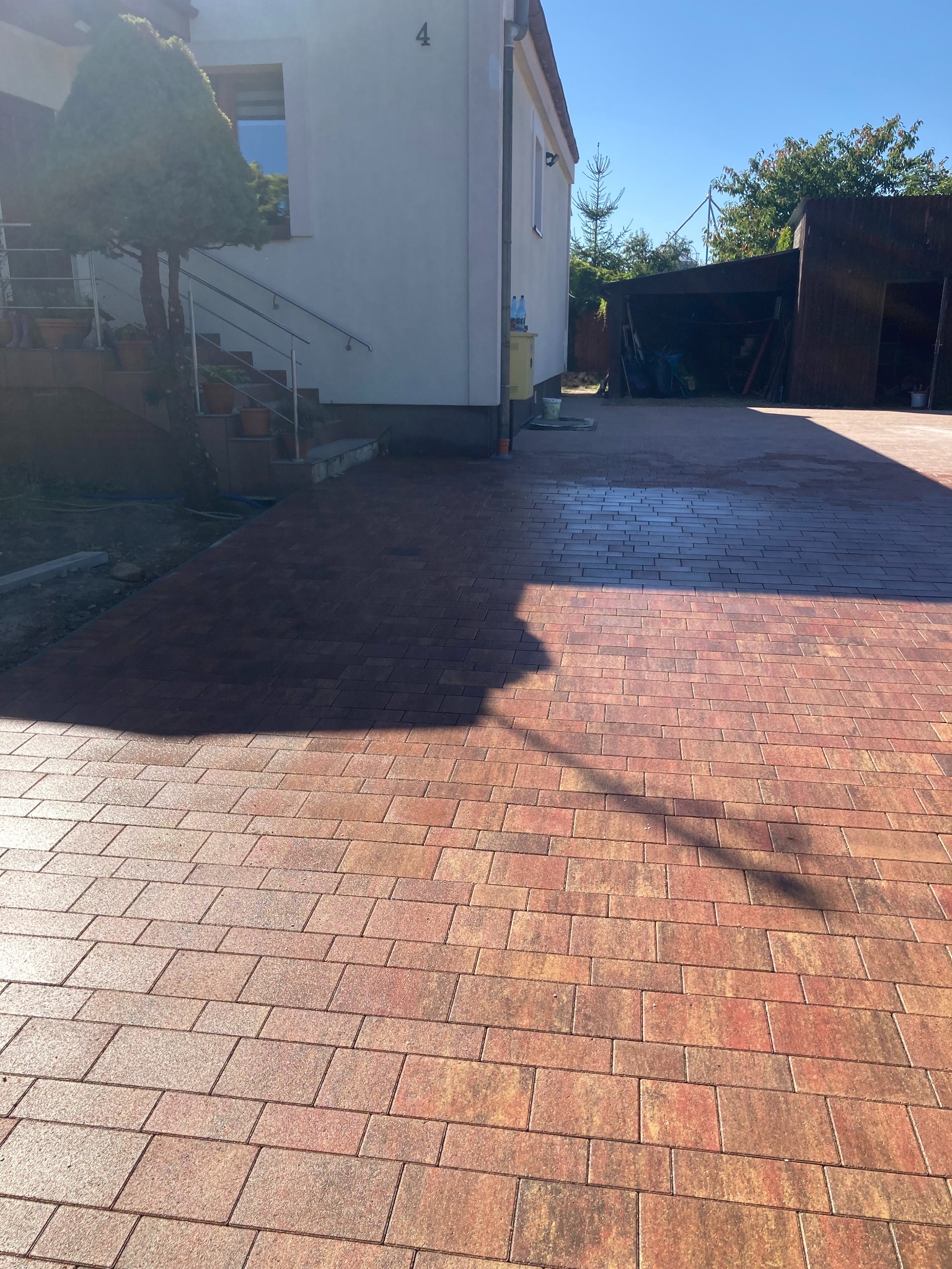 Nowo ułożona, czerwono-brązowa kostka brukowa na podjeździe przed domem z numerem 4, w tle widoczny garaż.