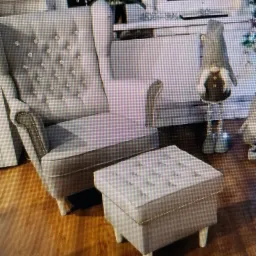 Elegancki, szary fotel typu uszak z pikowanym oparciem i podnóżkiem, wykończony srebrnymi detalami, na tle jasnego wnętrza z dekoracjami.