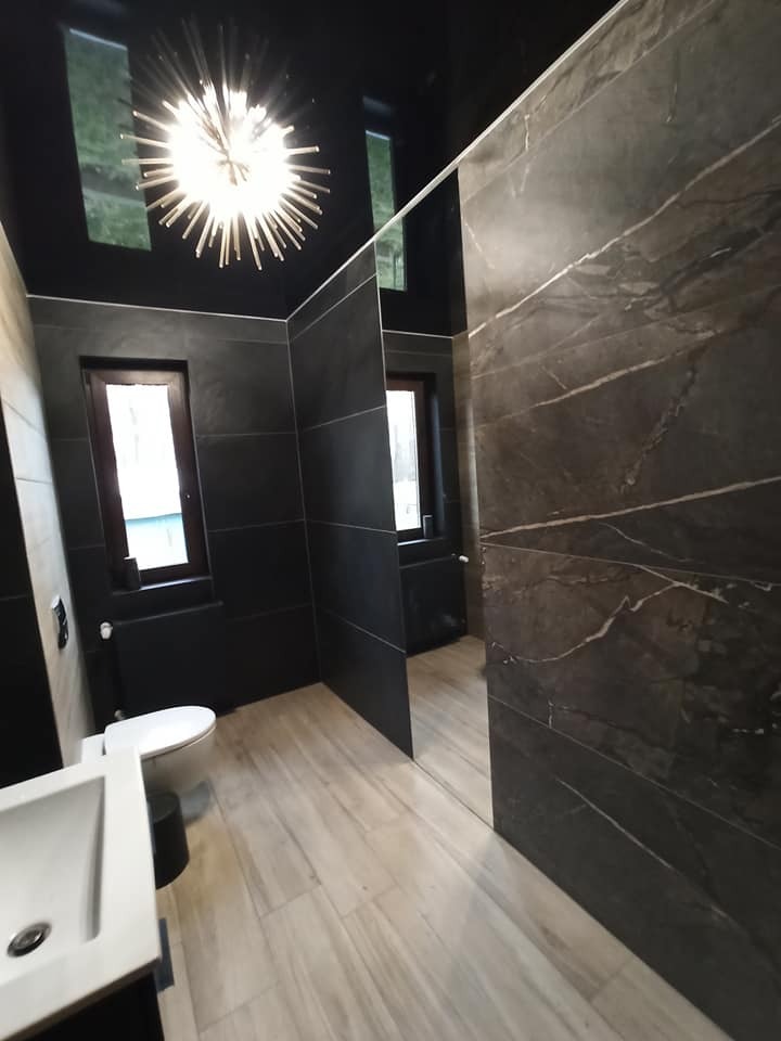 Nowoczesna łazienka z czarnymi płytkami, drewnopodobną podłogą i dekoracyjną lampą sufitową w kształcie gwiazdy.