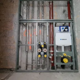 Stelaż instalacyjny Geberit Duofix z zamontowanymi rurami wodnymi i kanalizacyjnymi w surowym stanie, widoczne elementy przyłączeniowe z żółtymi zaślepkami.